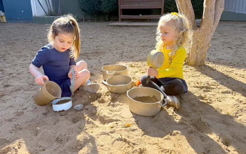 Duas meninas da Educação Infantil brincam com panelinhas no pátio de areia