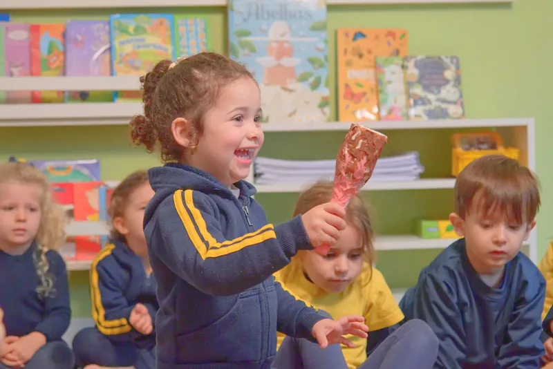 Menina ri com um brinquedo na mão, sentada com os colegas na sala